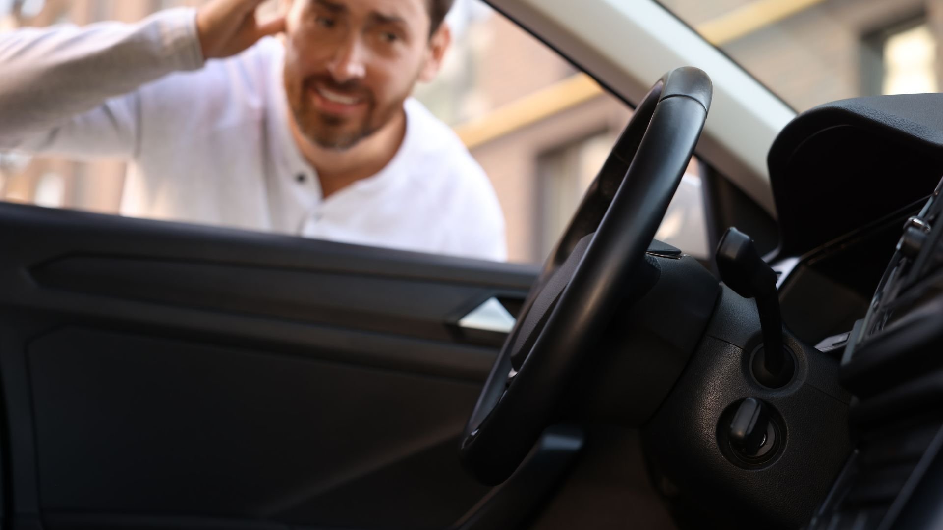 Person looking inside car through open window, steering wheel in view