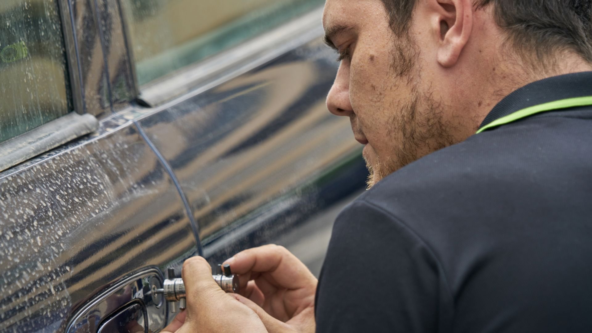 Person unlocking car door with key on rainy day, close-up view
