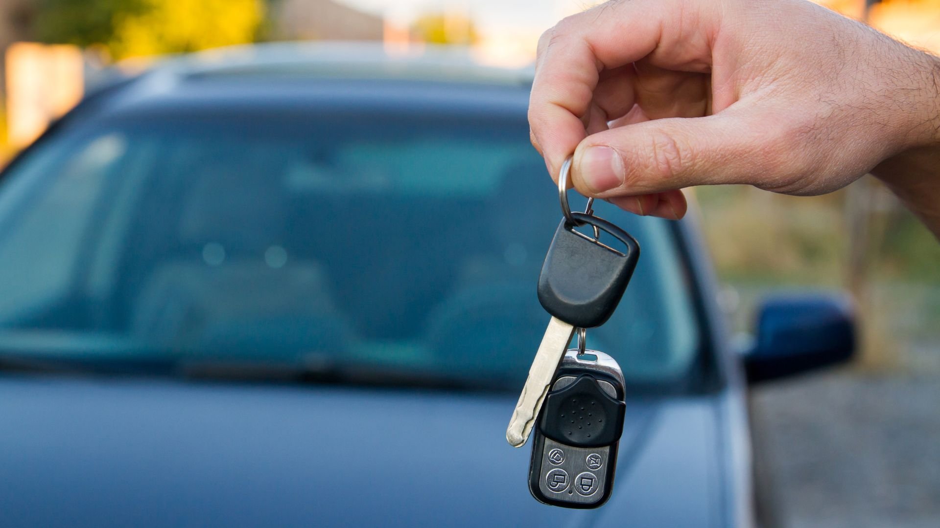 Hand holding car key with remote near blue vehicle